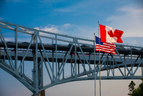 Blue Water Bridge, Port Huron, Michigan. West end of bridge over the St. Clair River connecting Sarnia, Ontario, Canada and the United States. Bridge is located at the extreme southern tip of Lake Huron. The flags of the USA and Canada waving in the foreground